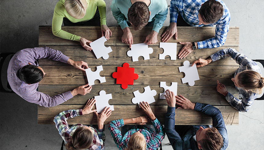 Eine Gruppe von Menschen sitzt an einem Tisch mit einzelnen Puzzle Teilen in der Hand