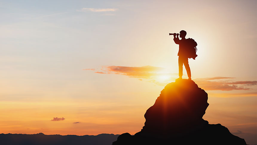 Eine Person schaut mit einem Fernglas von einem Berg aus in die Ferne